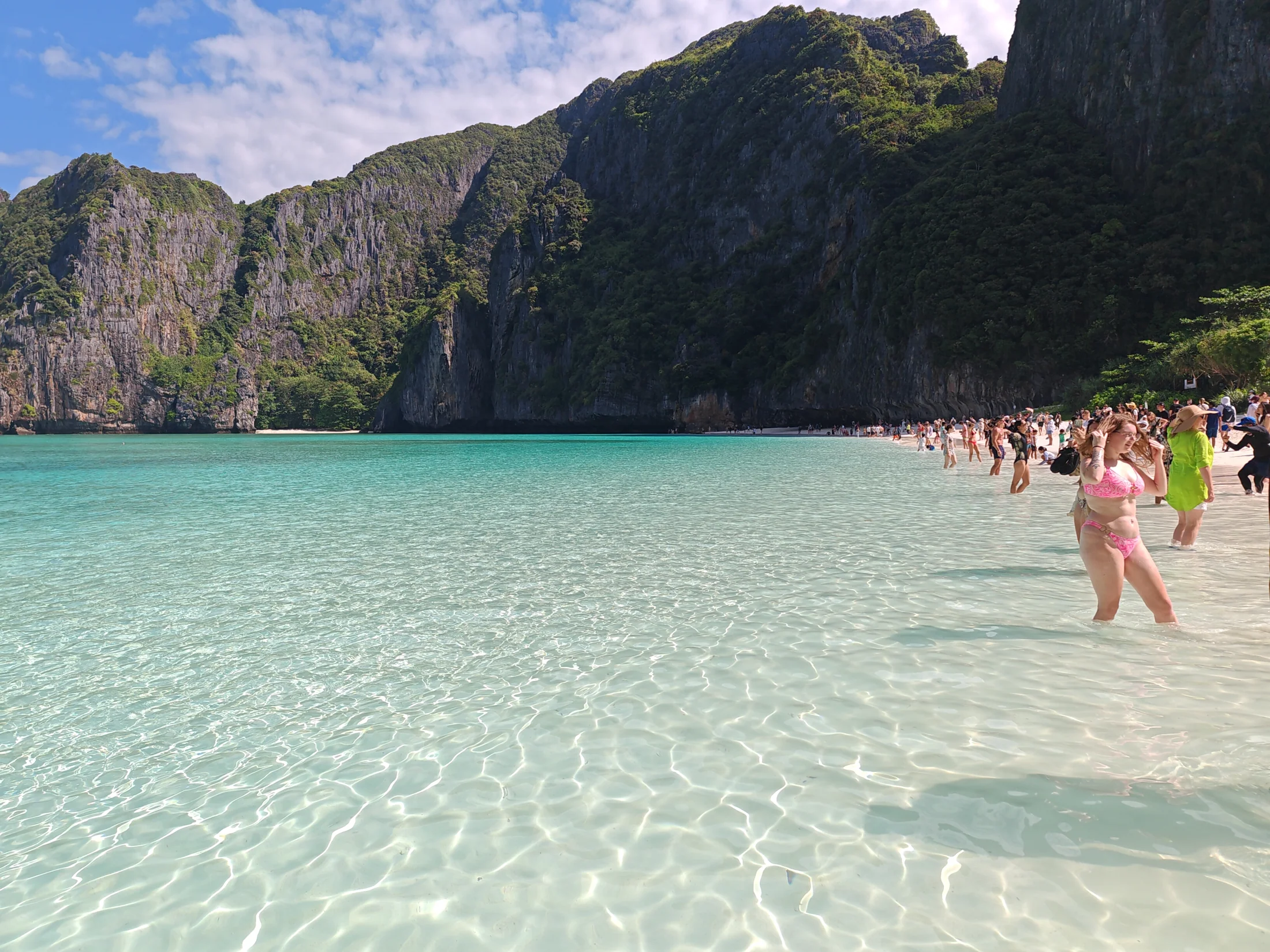 Clear shallow water and pale sand beneath tall limestone cliffs