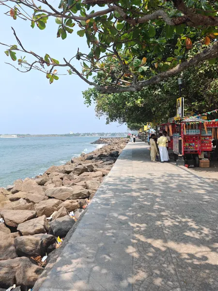 A shaded seafront walkway with rocks and open water beyond