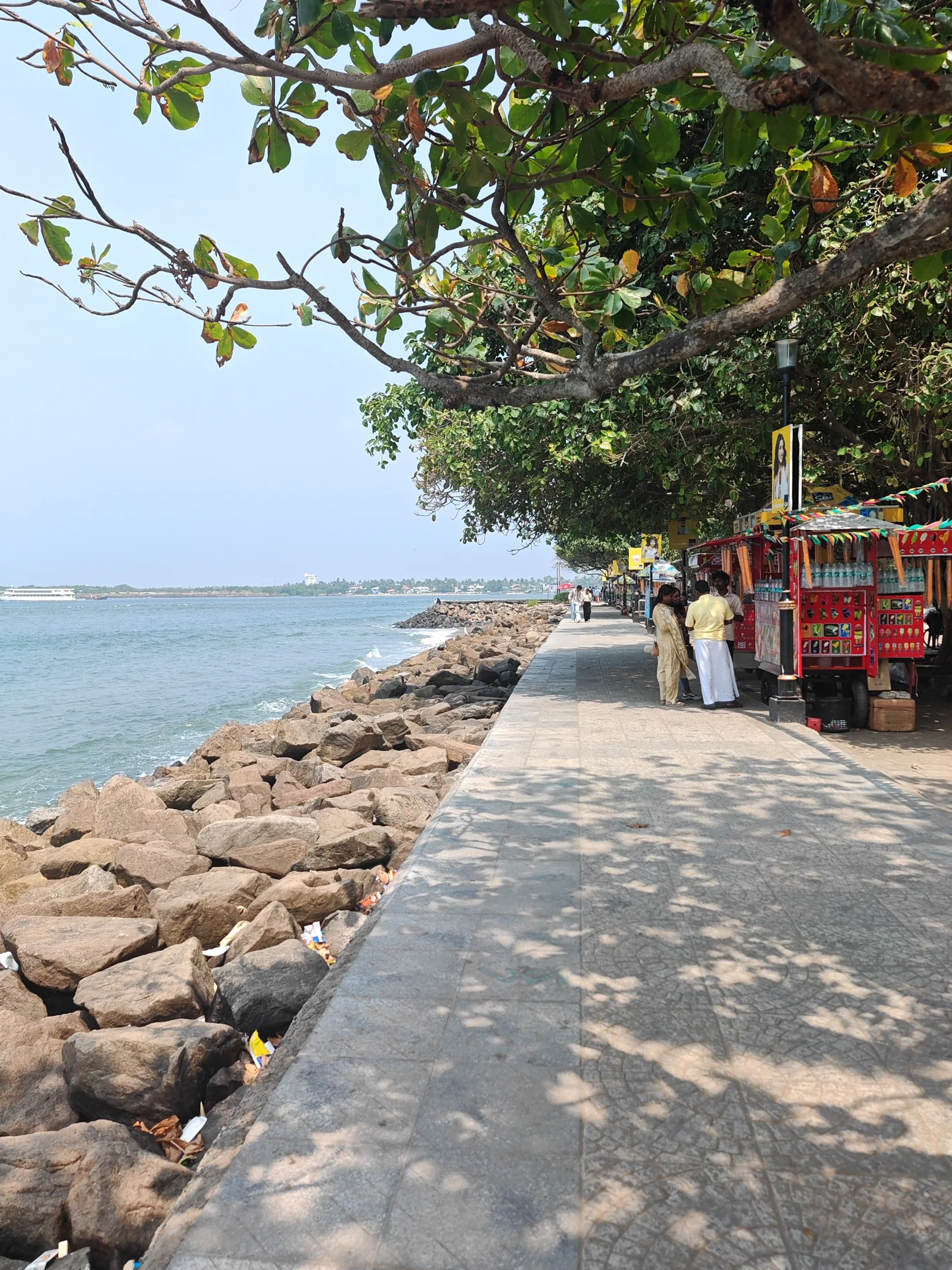 A shaded seafront walkway with rocks and open water beyond