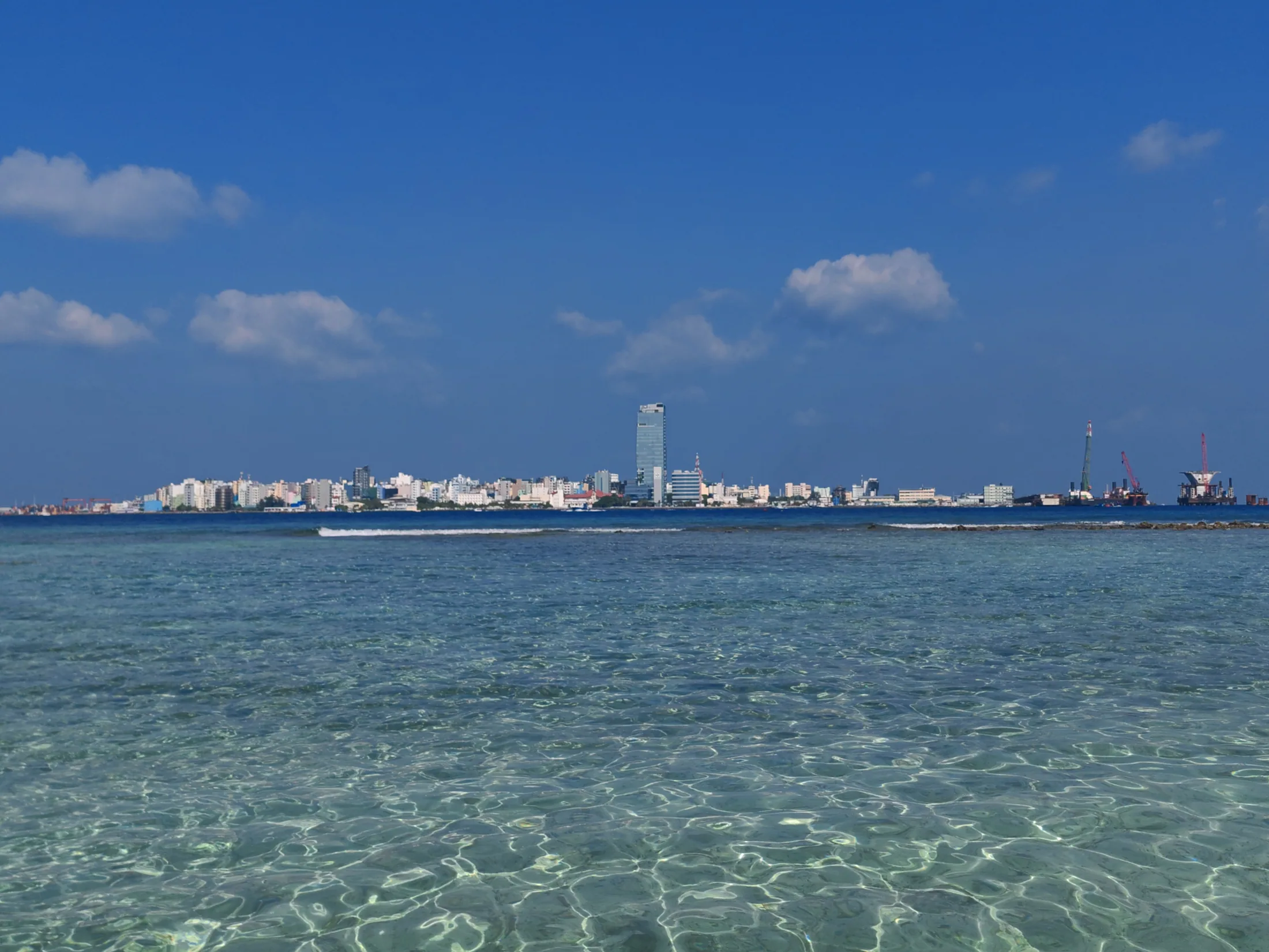 Clear shallows off Villingili with the Malé skyline across the water