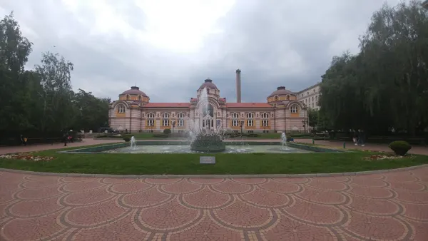 A formal garden and fountain before an ornate Sofia building