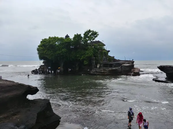 A tree-covered Balinese sea temple surrounded by waves