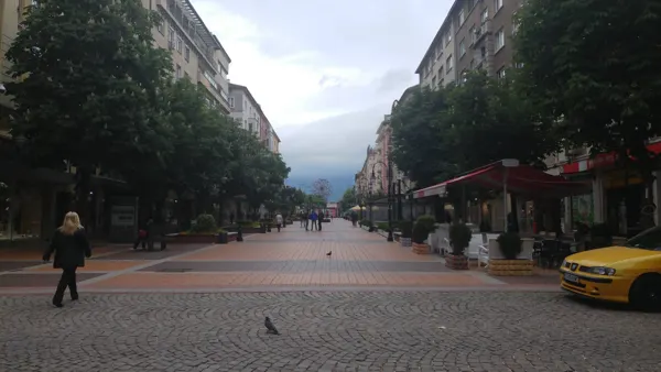 A broad pedestrian street leading between cafés and trees