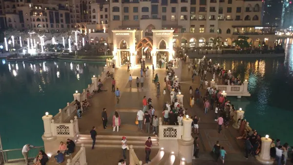 People crossing a lit bridge beside a Dubai waterfront