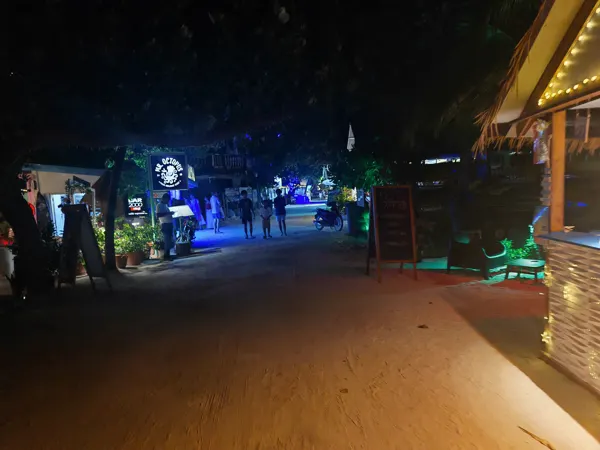 A sandy Maafushi street with cafés illuminated at night