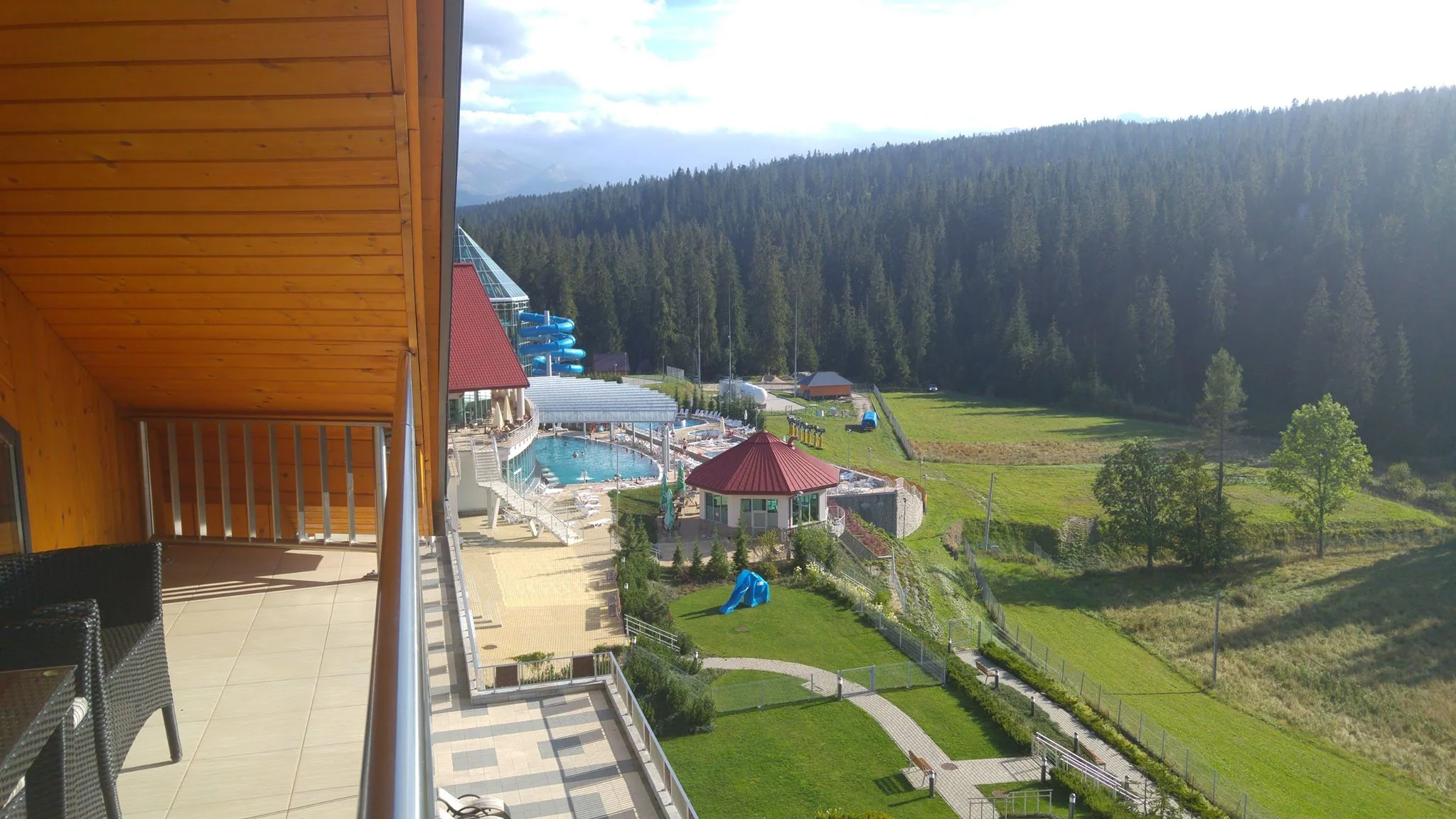 A balcony overlooking green grounds and a forested hillside