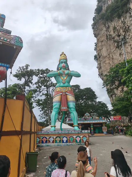 A large green Hanuman statue beside the limestone at Batu Caves