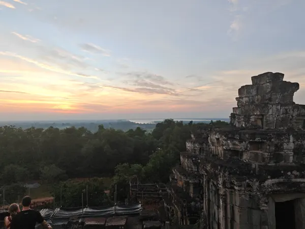 An ancient Angkor temple above the trees in warm evening light