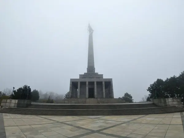 A tall memorial rising into mist above a paved terrace