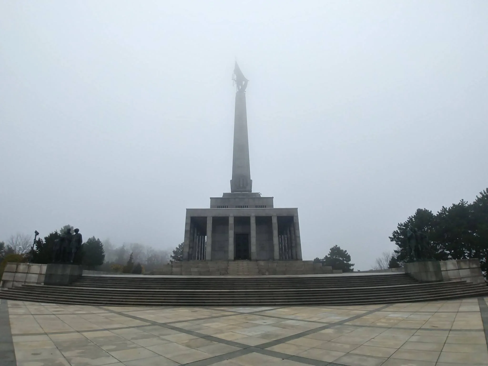 A tall memorial rising into mist above a paved terrace