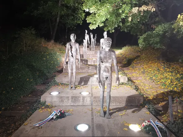 A line of memorial sculptures on steps beneath trees