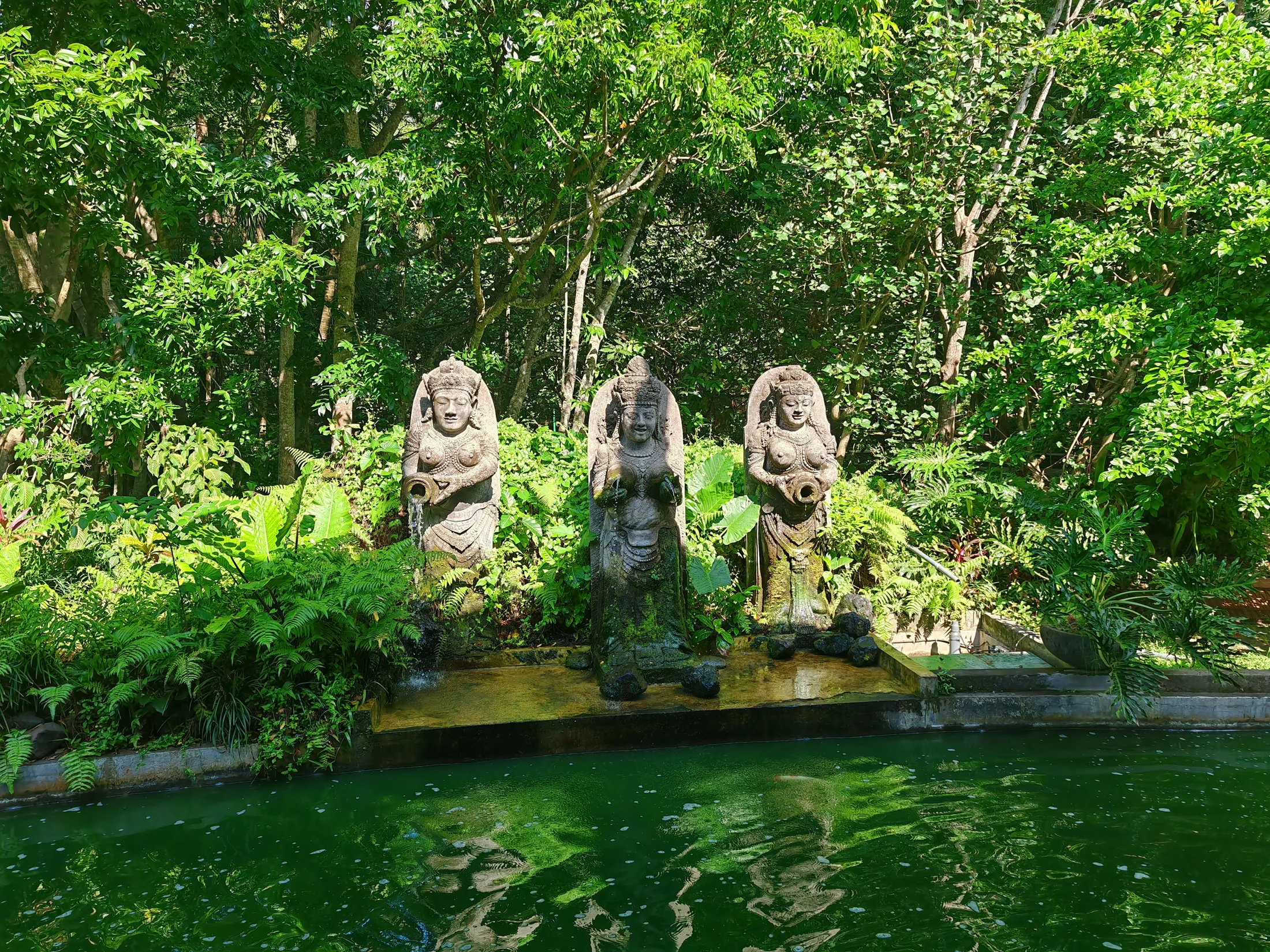 Stone figures beside a green pool in the forest at Ubud