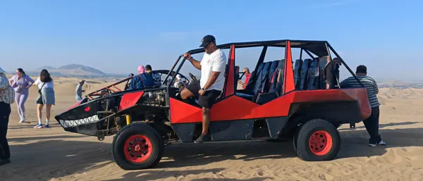 A traveller beside a red dune buggy in the Peruvian desert