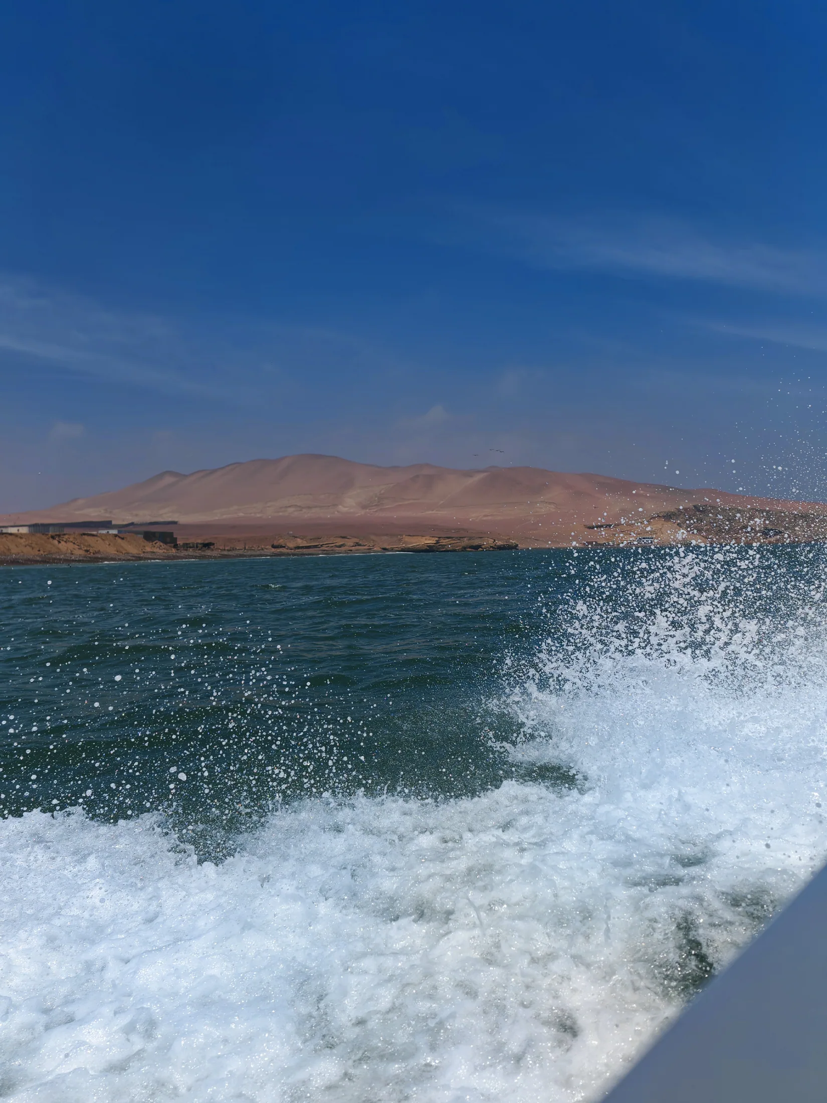 A boat’s wake beside the dry Peruvian coastline