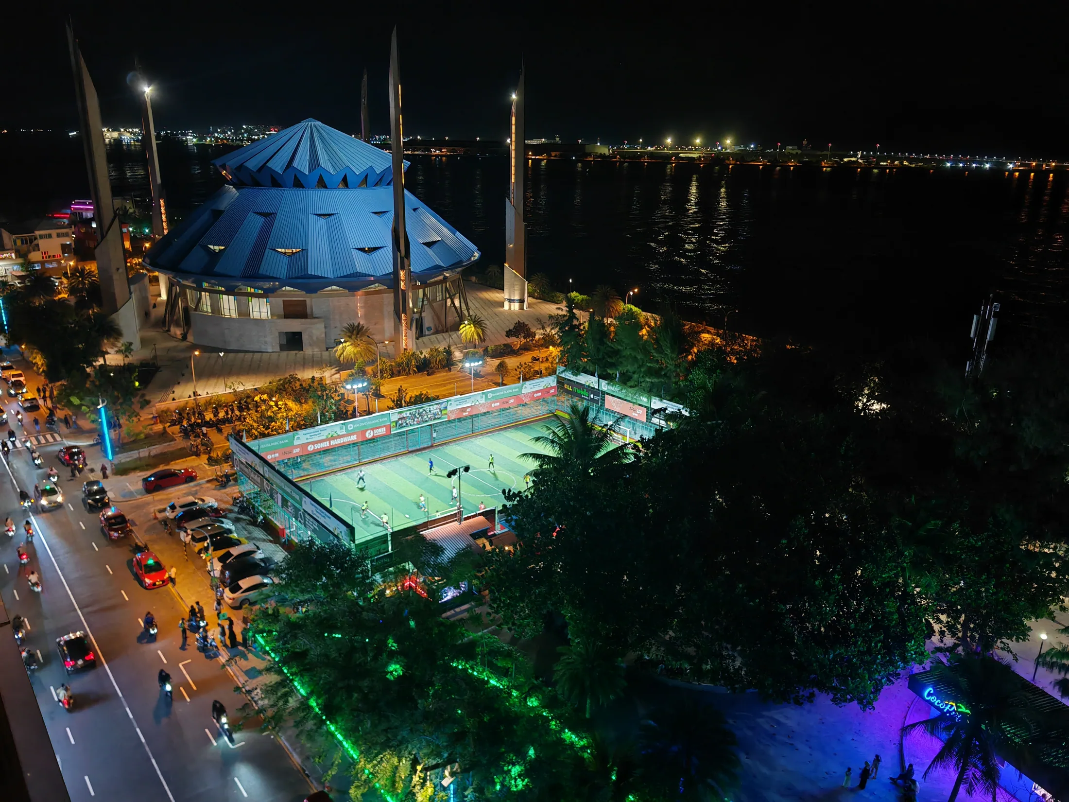 An illuminated mosque and waterfront seen from above in Malé