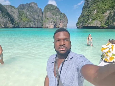 A traveller beside clear water and towering limestone cliffs