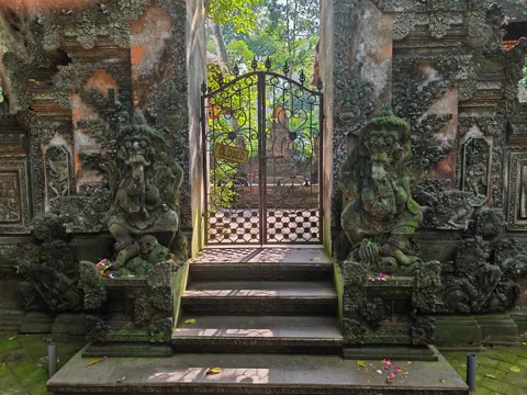 Carved stone figures and steps beside an ornate Balinese gate